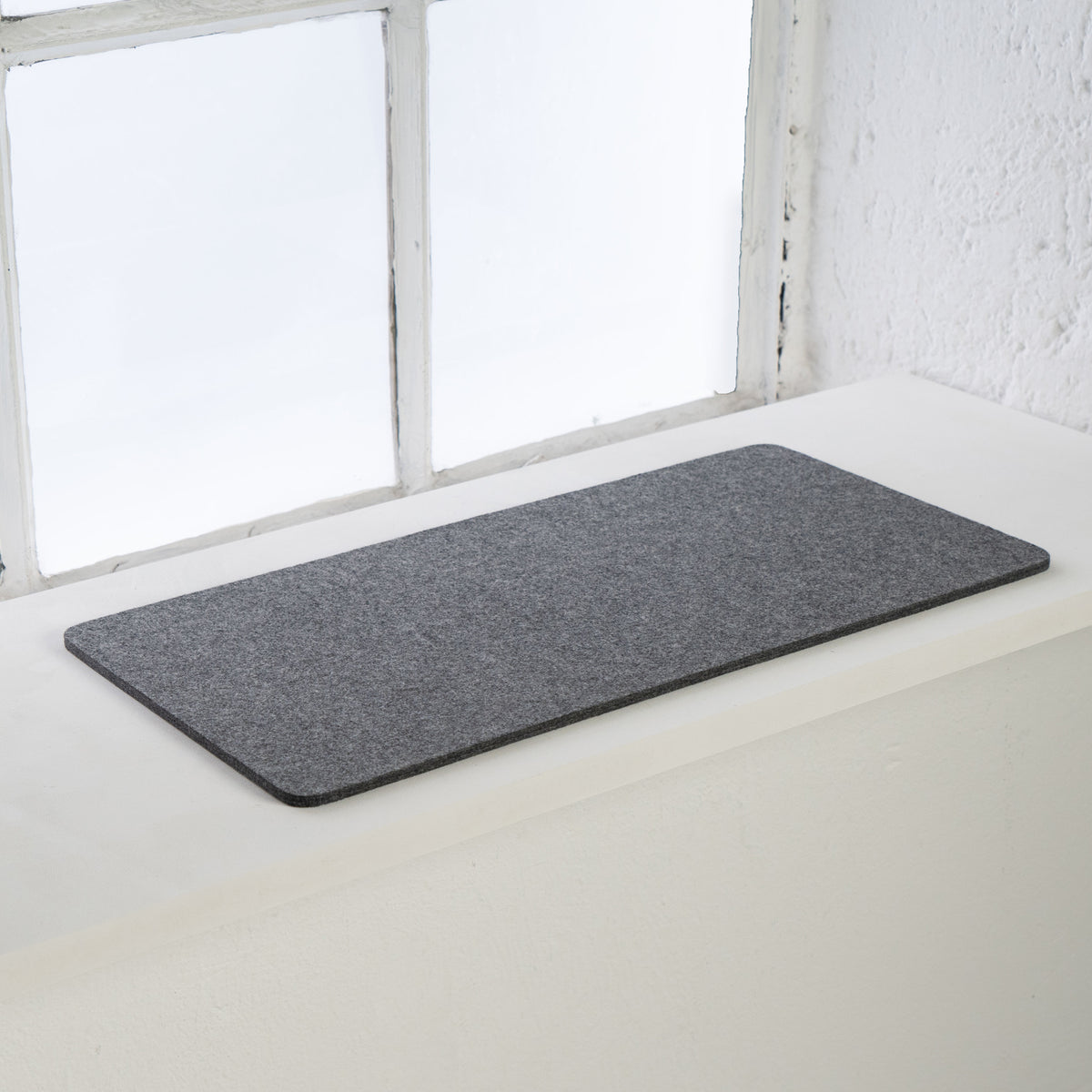 Anthrazitfarbene FELTY Fensterbrettauflage aus Wollfilz auf weißer Fensterbank