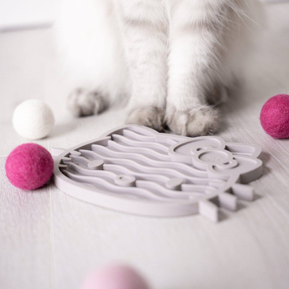 Katze steht vor ZENCAT Schleckmatte - Hello Kitty Edition in Taupe mit Filzbällen