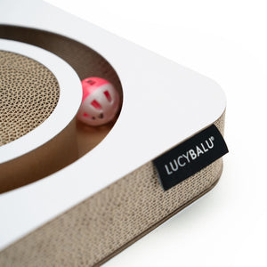 Nahaufnahme des LucyBalu PLAYBOOK Kratzbretts aus Wellpappe mit weißem Rahmen, sichtbarer Kratzfläche und integriertem rosa Spielball im Inneren