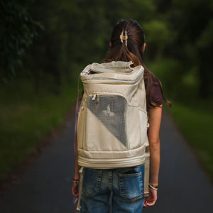 Sac à dos pour chat HOP-ON en sable, porté par une femme sur un chemin forestier, un chat regardant par la fenêtre en filet