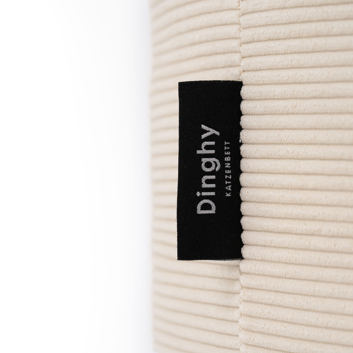 Cuccia per gatti DINGHY in bianco crema, primo piano dell'etichetta e della trama in velluto a coste