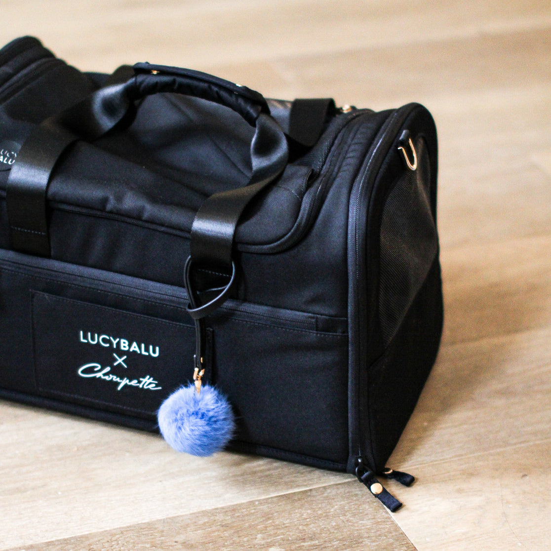 Nahaufnahme der schwarzen CHECK-IN Transporttasche Choupette Edition mit LucyBalu x Choupette Logo und blauem Pompon